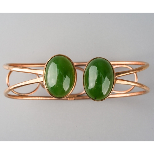 721 - A jade bangle. The torque design bangle set with two oval nephrite jade cabochons, rub over set, to ... 