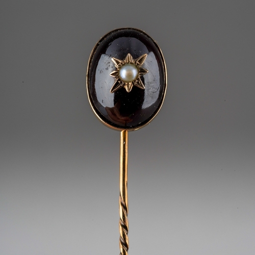 736 - A late 19th century garnet and seed pearl stickpin. Set with an oval garnet cabochon with split pear... 