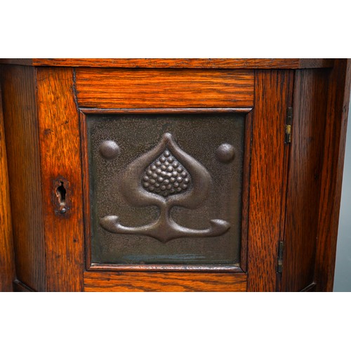 790 - An Arts & Crafts oak corner cabinet, the single door fitted copper panel embossed with a stylised ac... 