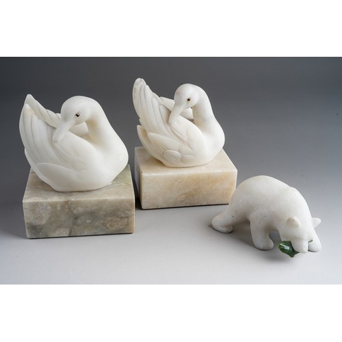 827 - A quartz model of polar bear with green glass fish together with a pair of carved marble swans (3)