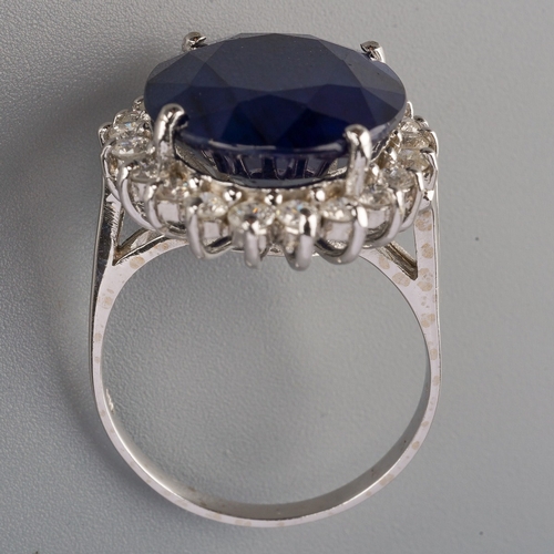 710 - A dress ring, set with an oval shape glass filled corundum, surrounded by round brilliant cut diamon... 