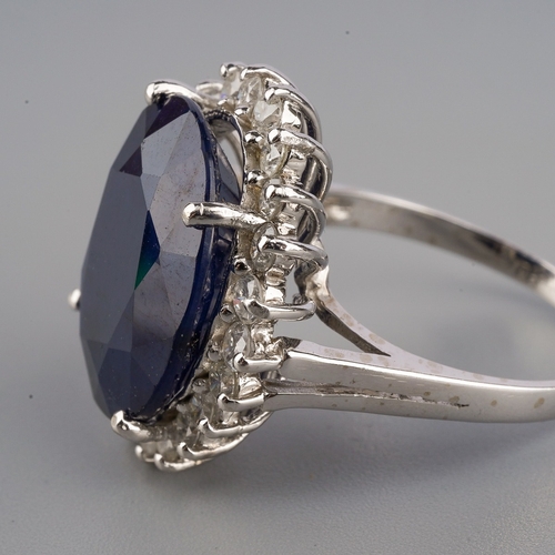 710 - A dress ring, set with an oval shape glass filled corundum, surrounded by round brilliant cut diamon... 