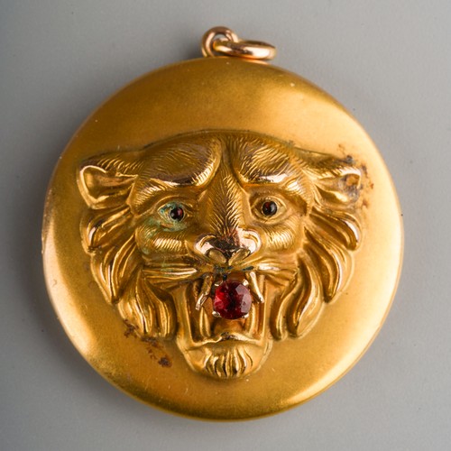 687 - A yellow metal circular locket, the front embossed in relief with a lion's mask with red stone caboc... 