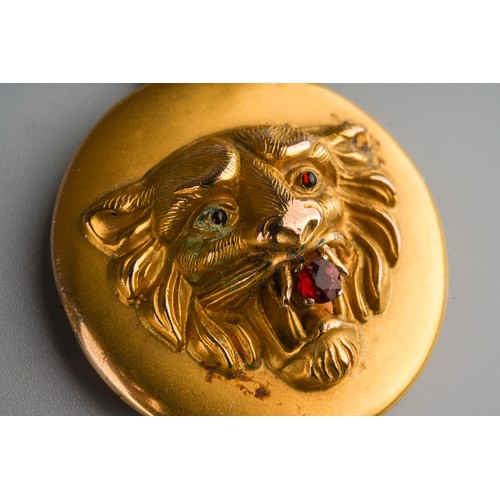 687 - A yellow metal circular locket, the front embossed in relief with a lion's mask with red stone caboc... 