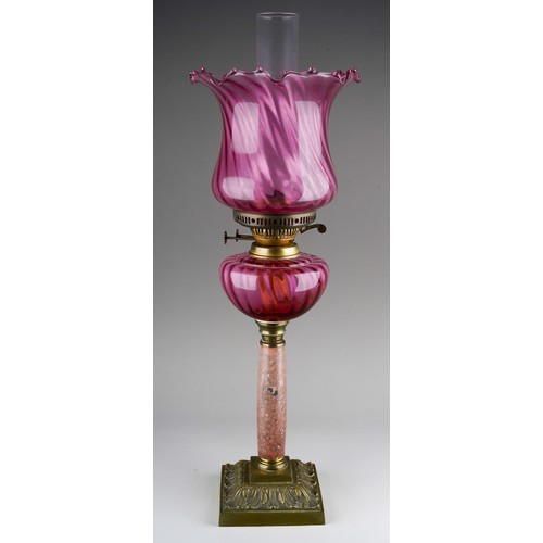 894 - An early 20th Century oil lamp with ruby glass wyvern twisted shade and reservoir, on mottled marble... 