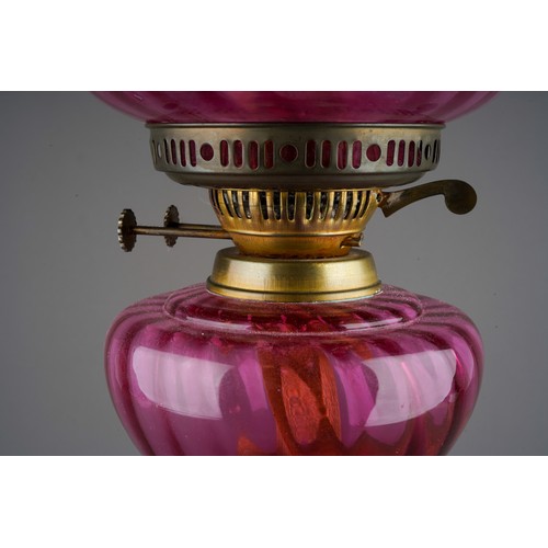 894 - An early 20th Century oil lamp with ruby glass wyvern twisted shade and reservoir, on mottled marble... 