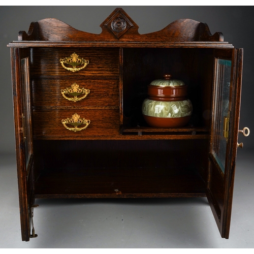 959 - An Edwardian oak smokers cabinet, raised back above bevel edge glazed double doors enclosing a shelf... 