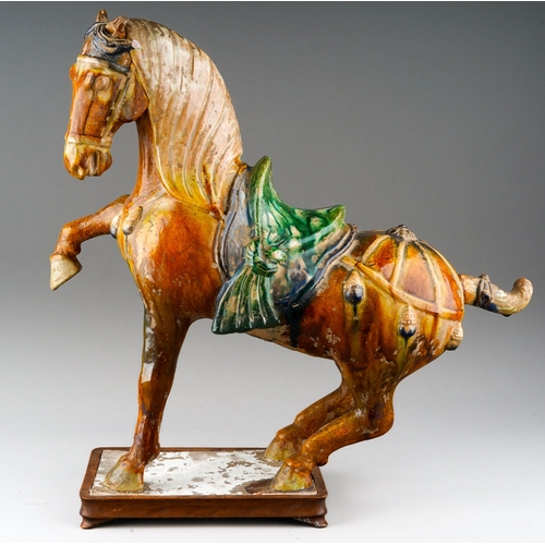 76 - A Tang Dynasty Chinese hollow pottery figure of a horse with one leg raised, the rectangular base wi... 