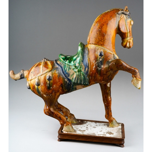 76 - A Tang Dynasty Chinese hollow pottery figure of a horse with one leg raised, the rectangular base wi... 