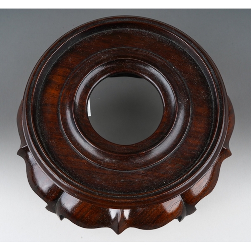 139 - A Chinese hardwood two piece stand, the turned circular top with short foot on a wavy lotus style ba... 