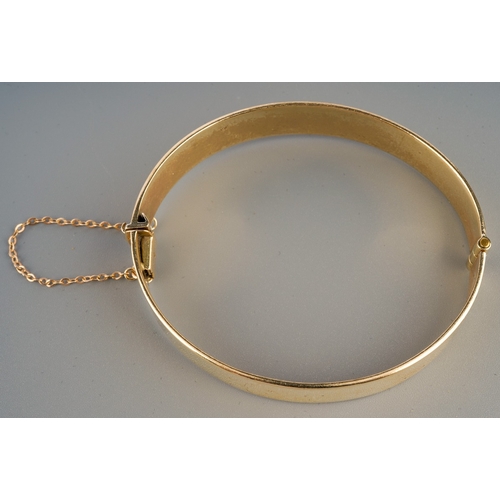 528 - A 9ct gold plain bangle, hinged, fitted with safety chain, stamped 375 BREV, inner dimensions 57mm x... 