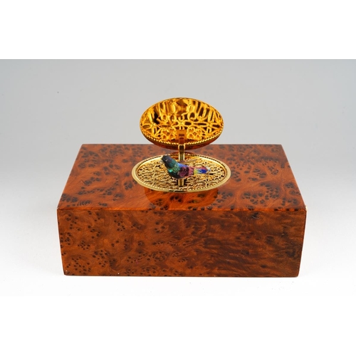 A cased Charles Reuge Swiss singing bird automaton in burr wood box, model no. T26875 B0433, winding mechanism to the underside, operating button to right hand side, the oval cover opens to reveal a filigree mount with bird, moving beak and wings, operating correctly, in good overall condition, width 12cm x depth 7.5cm x 4cm, the original storage case in poor condition, comes with assorted paperwork including operating instructions and a book about Music Boxes by Gilbert Bahl (2)