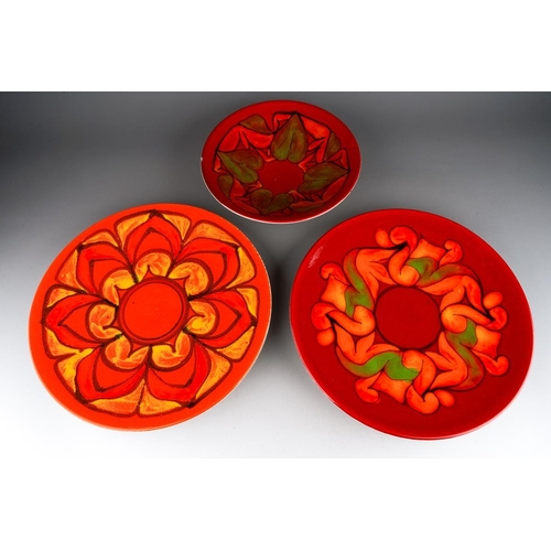 56 - Two Poole Pottery Delphis chargers, shape no 5, one in red, orange and green colourways, the other i... 