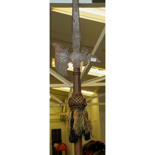 A replica halberd on a wooden shaft, fabric and tassel worn and ...
