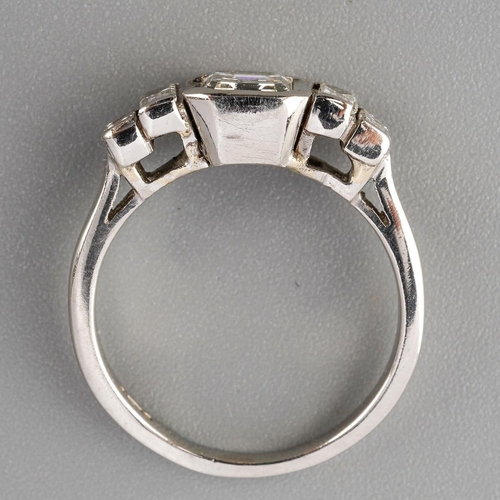 52 - A platinum diamond dress ring. Set with a principal emerald-cut diamond, rubover set, to the baguett... 