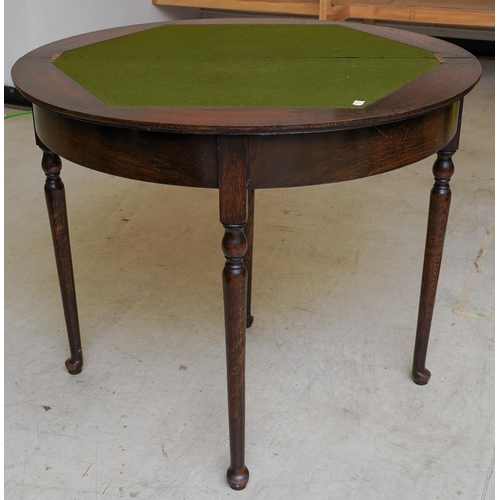 59 - An early 20th century dark stained oak demi lune card table, the fold over top with baize lining, on... 