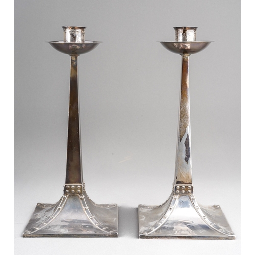 A pair of Arts & Crafts silver candlesticks after a design by Jan Eisenloeffel Amsterdam School, each with tapered stems with flared concave drip pan on square form base with rivetted detail, hallmarked by James Dixon & Sons, Sheffield, 1904, stamped Aird & Thompson Silversmith Glasgow, height approx. 22cm, filled [2]
