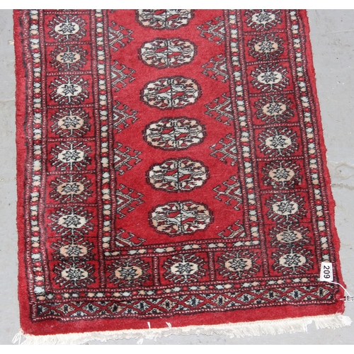 209 - A red ground runner rug, believed to be hand made decorated with gul medallions - likely Afghan