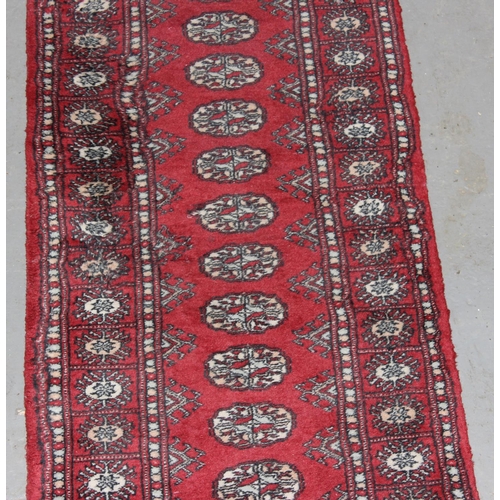 209 - A red ground runner rug, believed to be hand made decorated with gul medallions - likely Afghan