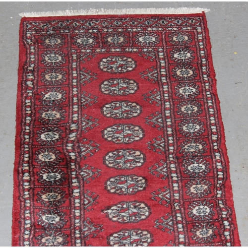 209 - A red ground runner rug, believed to be hand made decorated with gul medallions - likely Afghan