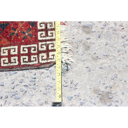 202 - An unusual antique red ground rug with latch hook border - possibly a prayer rug