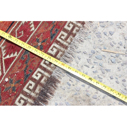 202 - An unusual antique red ground rug with latch hook border - possibly a prayer rug