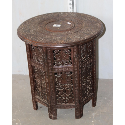 12 - An Indian hardwood table, heavily carved top with brass inlay and raised a folding carved octagonal ... 