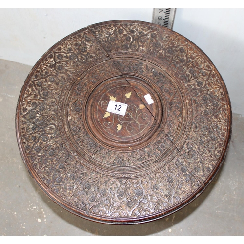 12 - An Indian hardwood table, heavily carved top with brass inlay and raised a folding carved octagonal ... 