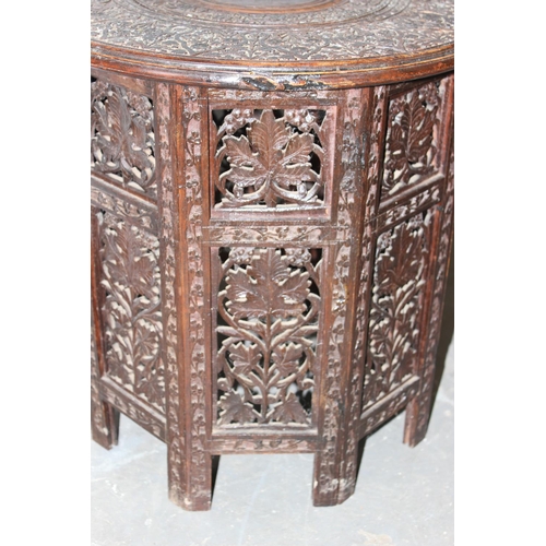 12 - An Indian hardwood table, heavily carved top with brass inlay and raised a folding carved octagonal ... 