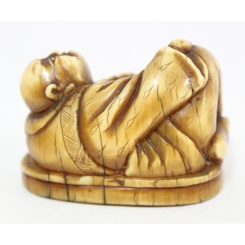 1601 - A Japanese carved netsuke depicting Hotei in laying pose, seemingly unsigned, approx 41mm wide