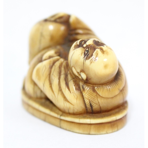 1601 - A Japanese carved netsuke depicting Hotei in laying pose, seemingly unsigned, approx 41mm wide