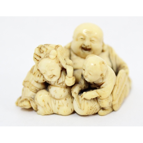 1603 - A Japanese carved netsuke depicting a seated male with 2 playing children, signed, approx 43mm wide