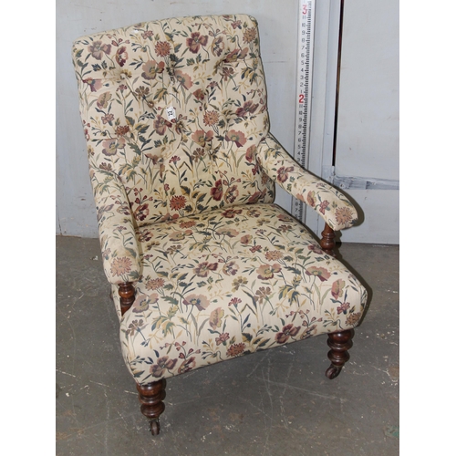 22 - An antique upholstered low armchair with floral upholstery standing on turned wooden legs with brass... 