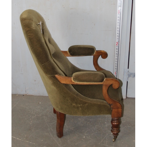 27 - An antique button backed armchair with green velvet upholstery and brass castors