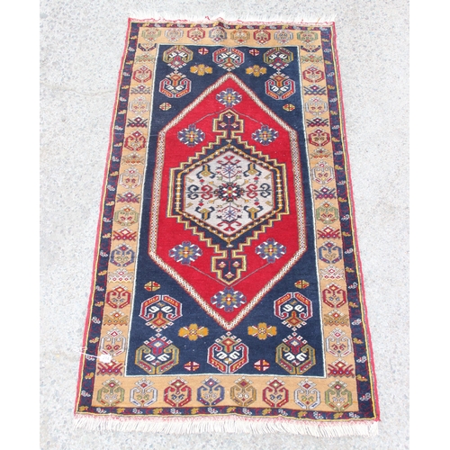 214 - A vintage hand knotted rug of blue ground with large red medallion and decorative cream border, appr... 