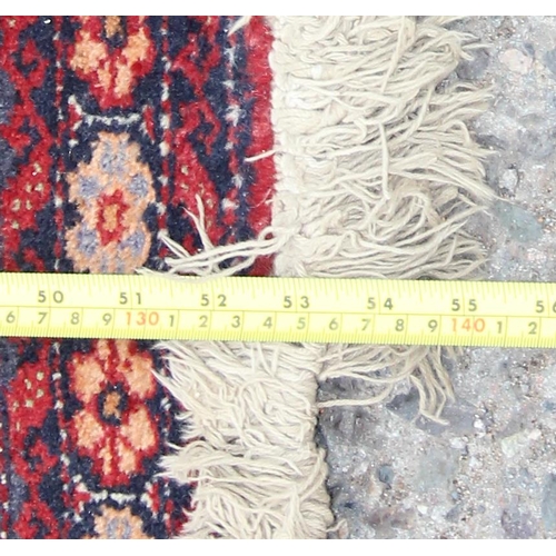 219 - A vintage hand knotted rug of red ground decorated with geometric gul, approx 140cm x 70cm