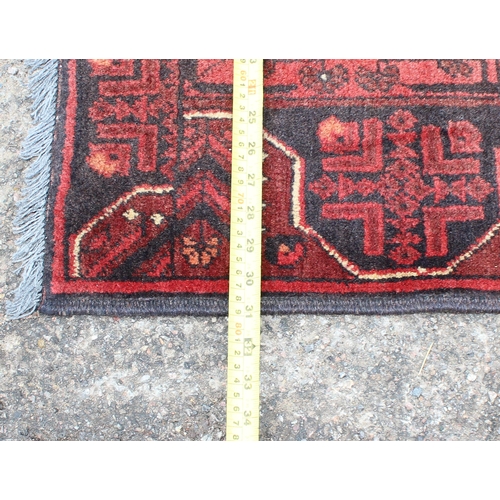 166 - A small handmade red and black ground rug, likely Turkish in origin, approx 120cm x 80cm