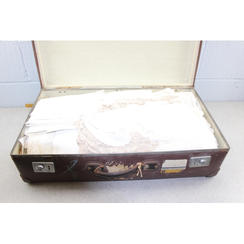 219 - A vintage brown suitcase containing linen and lace, other fabrics etc