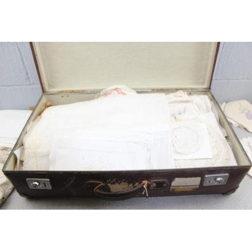 219 - A vintage brown suitcase containing linen and lace, other fabrics etc