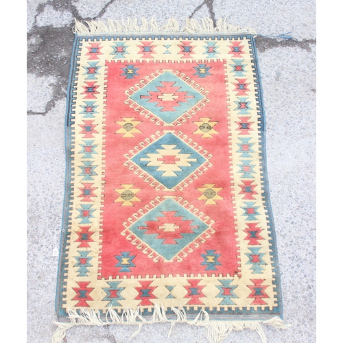 202 - A vintage red ground hand made wool rug with 3 central diamond medallions, approx 190cm x 118cm