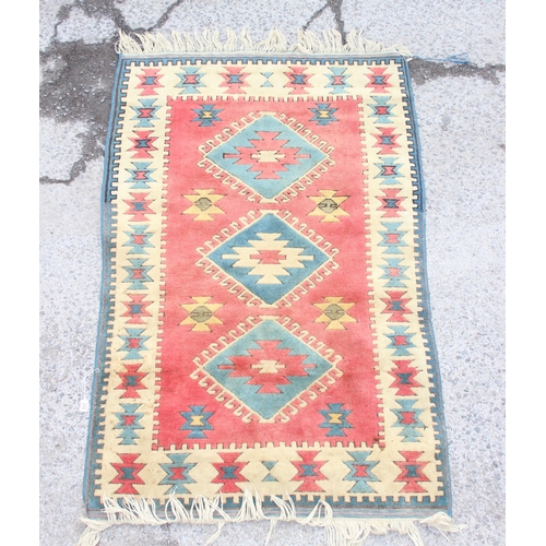 202 - A vintage red ground hand made wool rug with 3 central diamond medallions, approx 190cm x 118cm