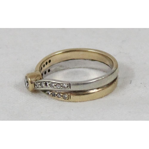 1128 - A 9ct white and yellow gold crossover ring set with a central diamond and flanked by smaller diamond... 