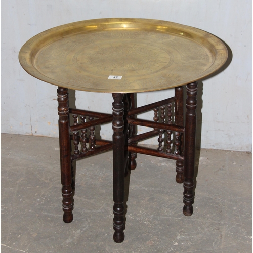 42 - A vintage Benares brass tray topped table with folding wooden base, the tray approx 65cm in diameter