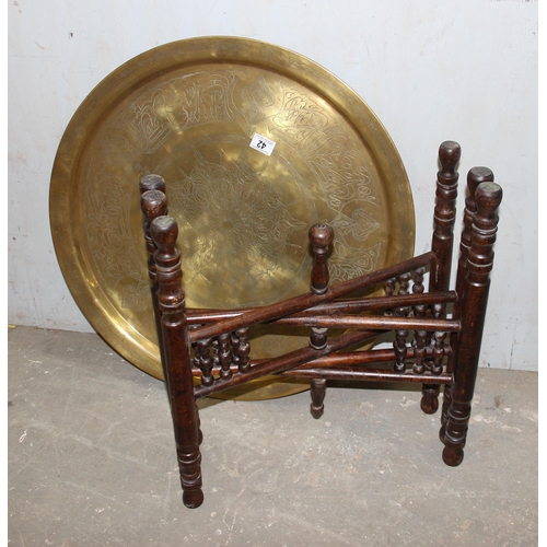 42 - A vintage Benares brass tray topped table with folding wooden base, the tray approx 65cm in diameter