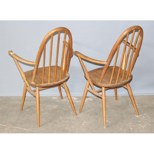 34 - A pair of blonde Ercol hoop backed carver chairs, one with remnants of a label, both with stamped ma... 