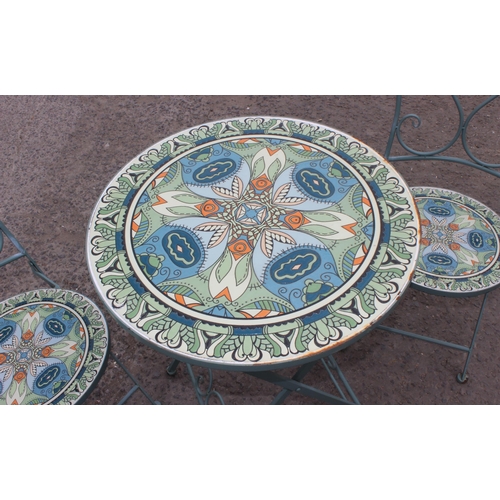 312 - A metal garden bistro set with 2 chairs, the table and chairs with colourful glazed pottery inserts,... 