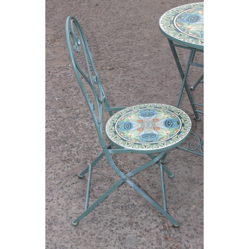 312 - A metal garden bistro set with 2 chairs, the table and chairs with colourful glazed pottery inserts,... 