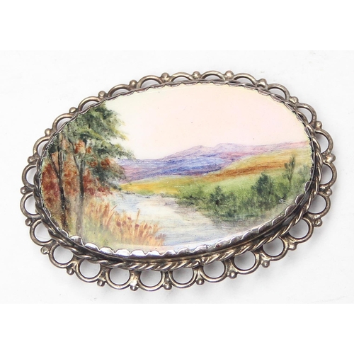 1138 - A silver mounted porcelain brooch set with a hand painted plaque of a river and mountain scene, appr... 