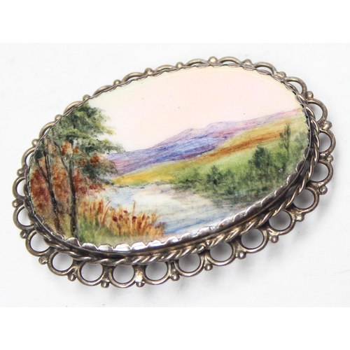 1138 - A silver mounted porcelain brooch set with a hand painted plaque of a river and mountain scene, appr... 