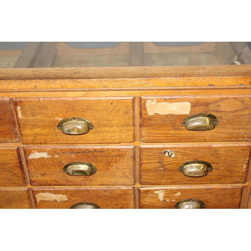 81 - An early 20th century light oak haberdashery shop counter or display cabinet with 30 drawers with br... 